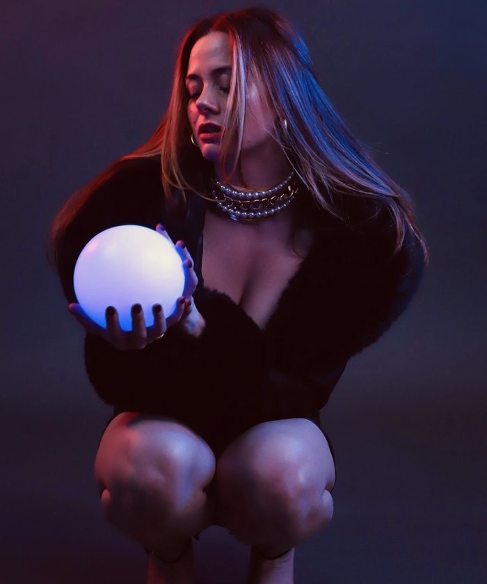 Hannah crouching in low violet light, holding a glowing orb